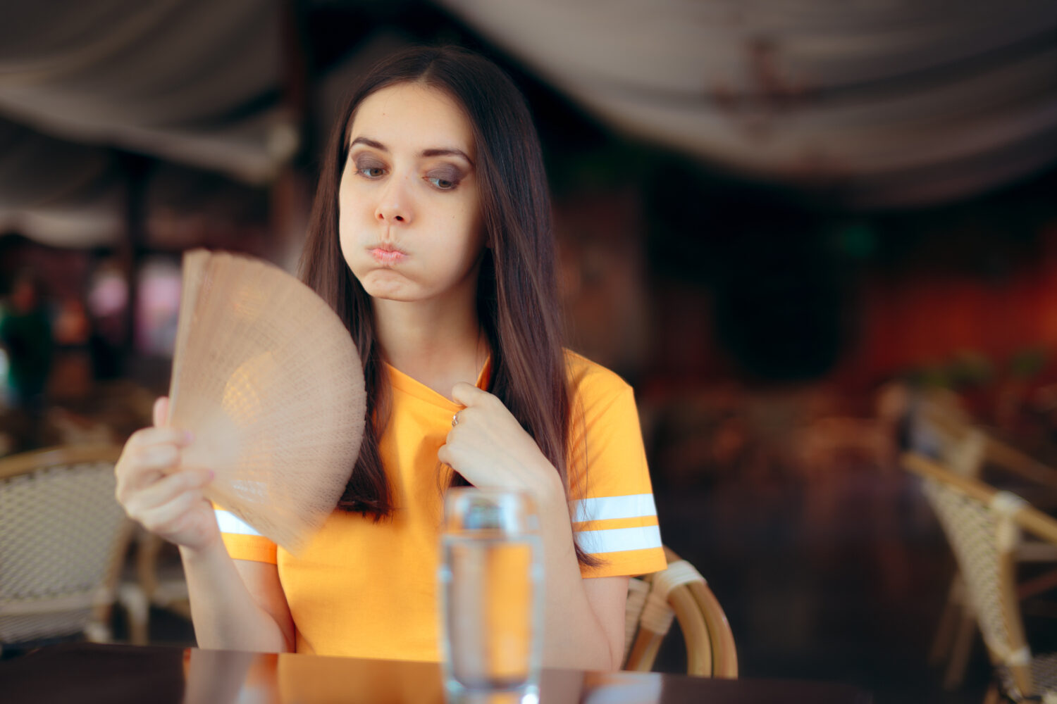 Woman in a Restaurant Fighting Heat Waves with a Fan
