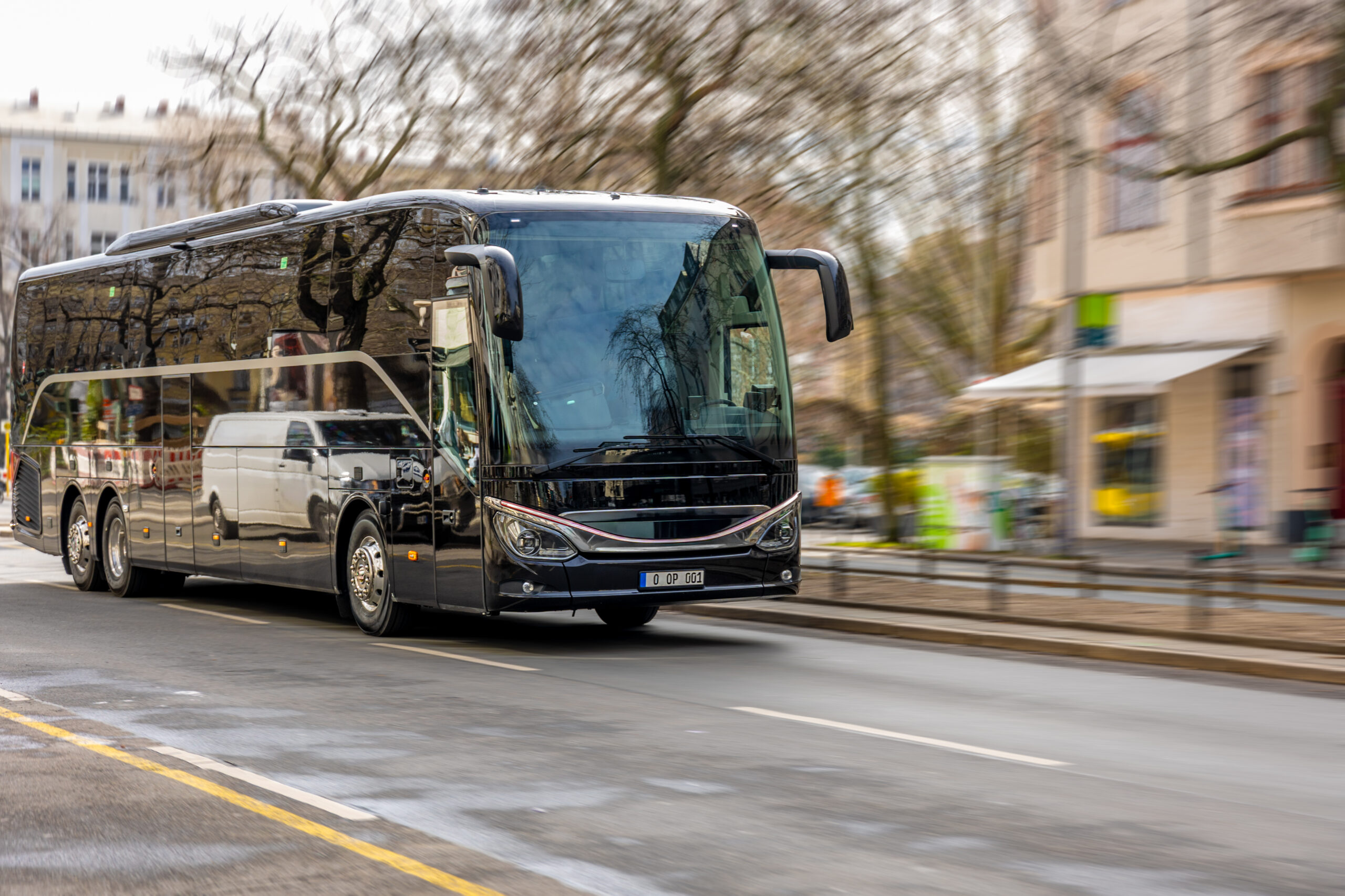 Black tourist bus driving on the road. Modern passenger coach moving through city.